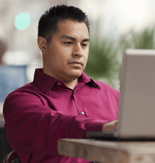 Business man looking down at his laptop while telecommuniting in an internet cafe